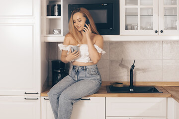 Food delivery, mobile shops, online shopping. A woman at home in the kitchen at the will of the refrigerator. A girl with a good figure holds a mobile phone in her hands.
