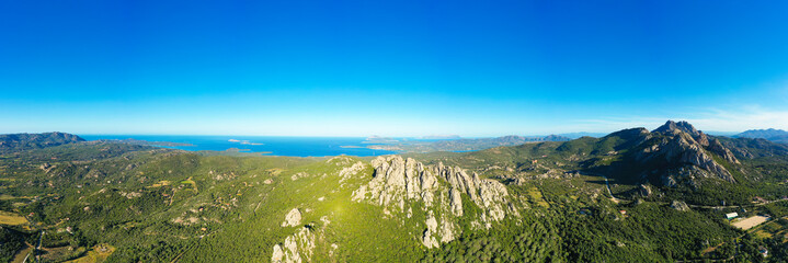 View from above, stunning aerial view of a valley surrounded by some granite mountains, green vegetation and the mediterranean sea in the distance. San Pantaleo, Sardinia, Italy.
