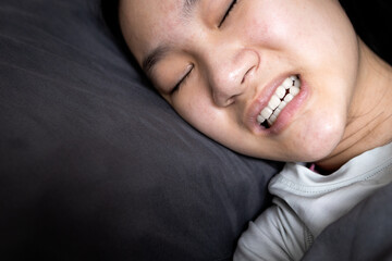 Asian child girl suffering from bruxism while lying in bed at night,female grinding of the teeth during sleep,teeth clenching,sleep disorders,oral health problems,dental care medical,bruxism concept - obrazy, fototapety, plakaty
