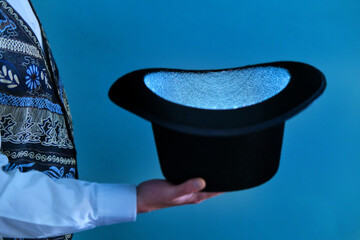 Hat in the hands of a magician on a blue background, close up