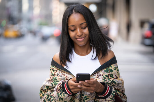 Young black woman in city walking street using cellphone