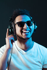 Smile Young African American man portrait wearing headphones and enjoy music over black Background. Blue light reflection on face.