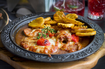 Baked potatoes, tomatoes, pork with rosemary and yellow cheese in metal plate on the table