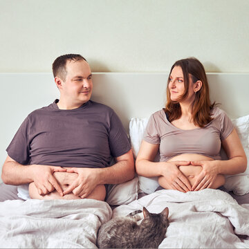 A man and a pregnant woman lie in bed holding their tummies, the concept of a sympathetic pregnancy
