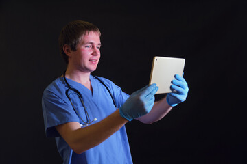 Doctor in blue uniform holds a digital tablet in his hands, black background