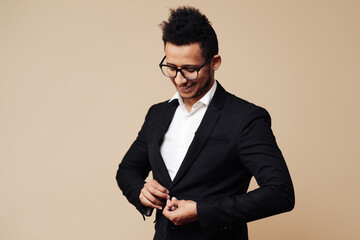 Portrait of young Afro businessman wearing shirt, black suit, glasses while standing at beige background.