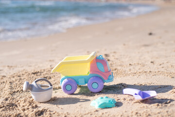 Children's beautiful delicate coloring toys car and watering can, shovel and mold placed on sand. Sandy seashore. Kid play on beach. Family’s vacation on sea. Summer time.