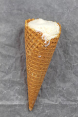 On the white crumpled paper there is a whole waffle cone with ice cream in the center