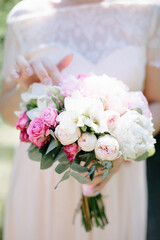 Round bouquet in hands of bride of pink roses and peonies with greenery. Selective focus.