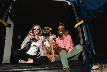 Hipster friends with dog celebrating with wine together in camper van during summer travel vacation - Main focus on african girl face
