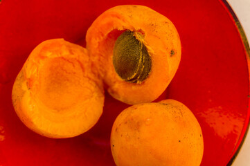 halves of a large fresh apricot on a red saucer, close-up