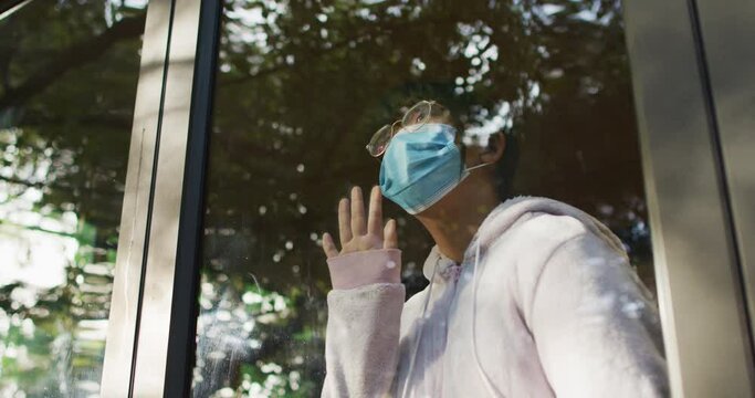 Asian girl wearing face mask and looking through window