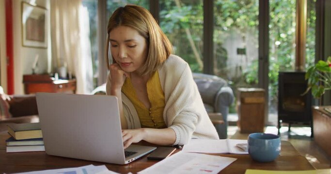 Asian woman sitting at table working from home and using laptop