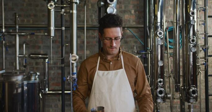 Portrait of happy caucasian man working at gin distillery using equipment and smiling to camera