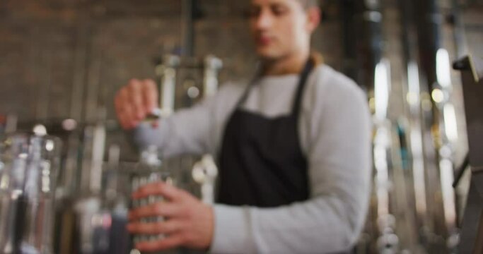 Caucasian man working at gin distillery, wearing apron, fastening lid on bottle of gin