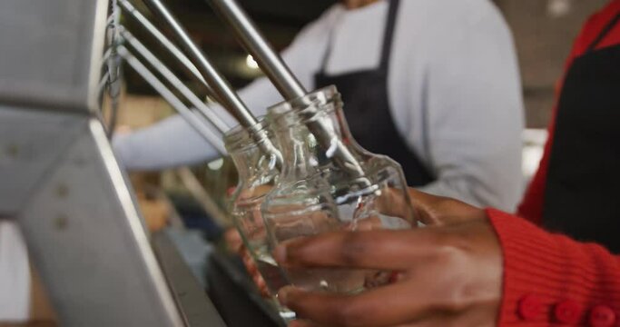 Midsection of two diverse colleagues at gin distillery filling and fastening lids on bottles by hand