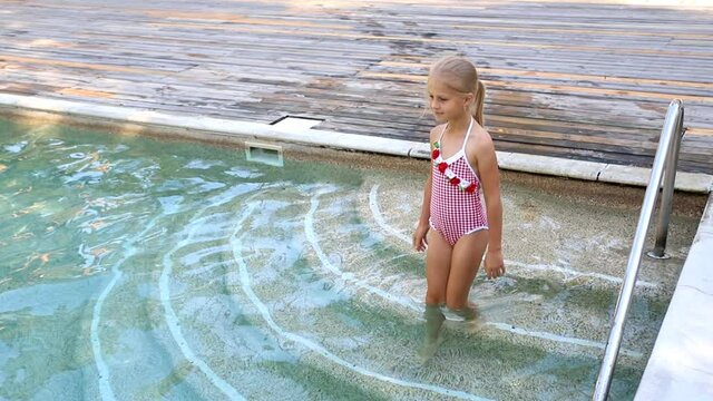 Little cute adorable blond playful beautiful caucasian active school girl enjoy swimming at pool edge at summertime outdoor sea resort area. Happy kid friend leisure vacation travel concept