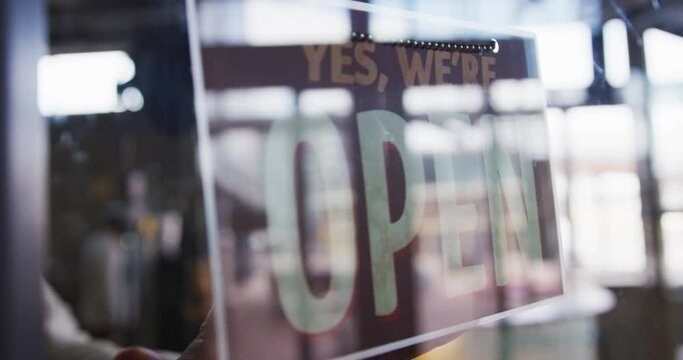 Close up of hands of female cafe owner changing closed sign to open in the window