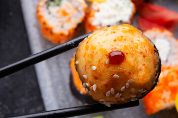 baked sushi roll holding by sticks. sushi rolls served at grey  tray. flat lay. close up