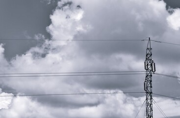 A black and white image of a high voltage pole with a sky and clouds background.
