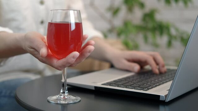 An evening with glass wine. A woman pas her work time by computer with a glass of wine in the room.