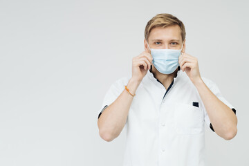 Portrait of a young male medical doctor putting sterile mask isolated on white background with copy space