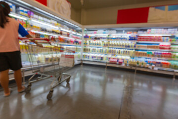 Defocused blur of female cart buying milk in supermarket