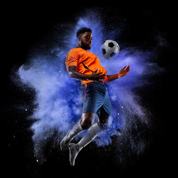 One young sportsman soccer football player in explosion of colored neon powder isolated on dark background