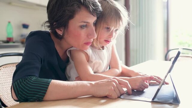 Mom and child daughter indoors at home using tablet together watching cartoon