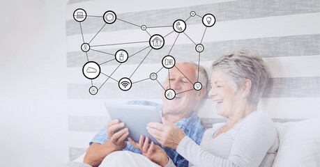 Composition of digital icons over happy senior couple using tablet in bed