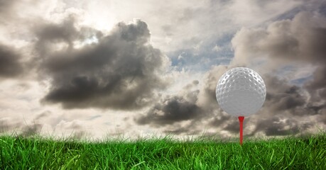 Composition of golf ball in grass on red tee, clouds, and copy space