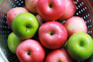 Top view of washed red and green apples in a basket, they still look wet.