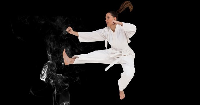 Composition of female martial karate artist with white belt in the air over smoke and copy space