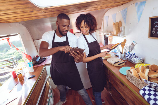 Diverse couple behind counter using tablet in food truck