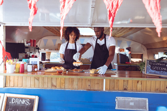 Diverse couple preparing hot dogs behind counter in food truck