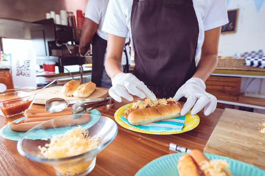 Mixed race woman garnishing hot dog behind counter in food truck