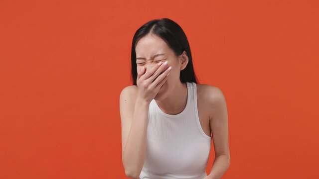 Excited cheerful funny young asian woman 20s years old wears white tank top shirt look camera laugh smiling watch comedy movie pointing index finger on you isolated on orange color background studio