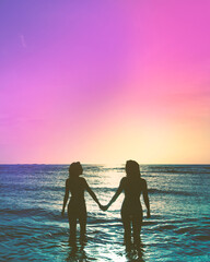 Fototapeta premium Two friends holding hands at the beach at sunset in the ocean