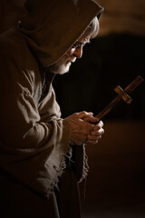 Old poor monk looks at the cross and doubts