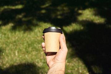 Craft paper cup with coffee in man hand. Time for drinking coffee in the city. Disposable paper cup closeup. Blank space for text, mockup. Concept of coffee to go, takeaway drinks, morning snack