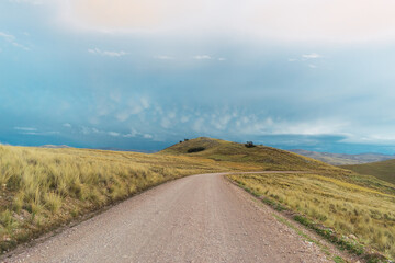 Fototapeta premium dirt road in the Andes of Peru with a blue sky and gray clouds at sunset surrounded by straw from the mountains