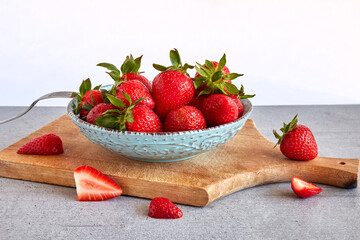 Red strawberries in a plate with a fork on a cutting board on a concrete background