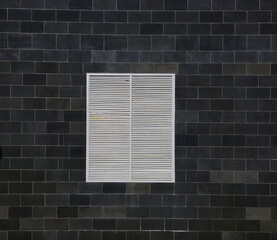 A barred ventilation window in the black-tiled wall