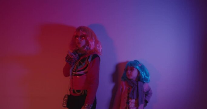 Two little girls blowing kiss wearing a colorful wig and heart-shaped sunglasses posed for a photo shooting on the disco light background