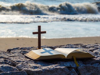 Holy Bible and wooden cross on stone with wave blue sea as background. Faith miracle heaven. Love study bible. Book of life. Christian Pray, Worship praise concept. Believe Jesus forgiving heart.  - obrazy, fototapety, plakaty
