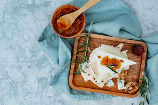 Overhead view of a rustic cheese board with a stack of blue cheese, cheddar, goats cheese, walnuts and grapes