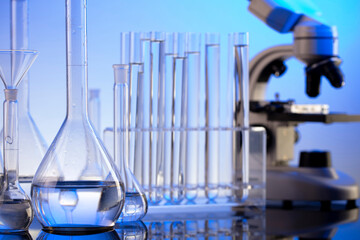 Laboratory investigations. Microscope, glass tubes and beakers on blue background.