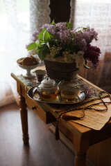 A bouquet of lilacs on the table, a cup of tea on a tray.