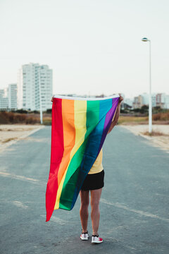 Woman runner with rainbow flag on her back in the street. Gay Pride. LGBT