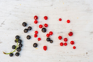 Berries red and black currants with strawberry are scattered on the old wooden table